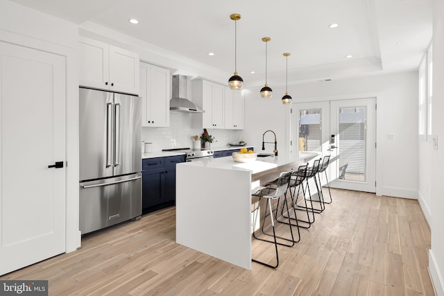 kitchen with light wood finished floors, light countertops, french doors, high end refrigerator, and wall chimney range hood