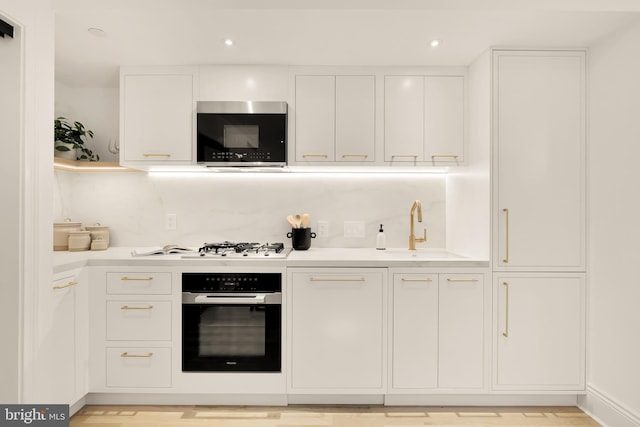 kitchen with oven, a sink, stainless steel microwave, white cabinets, and light countertops