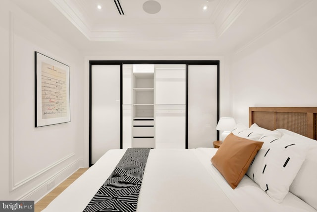 bedroom with wood finished floors, a tray ceiling, recessed lighting, a closet, and crown molding