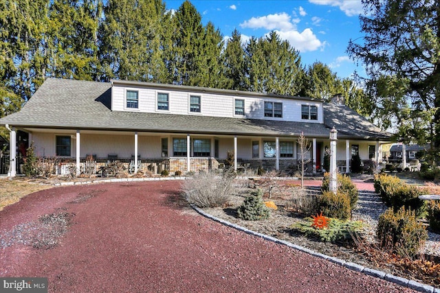 farmhouse with a porch, roof with shingles, and dirt driveway