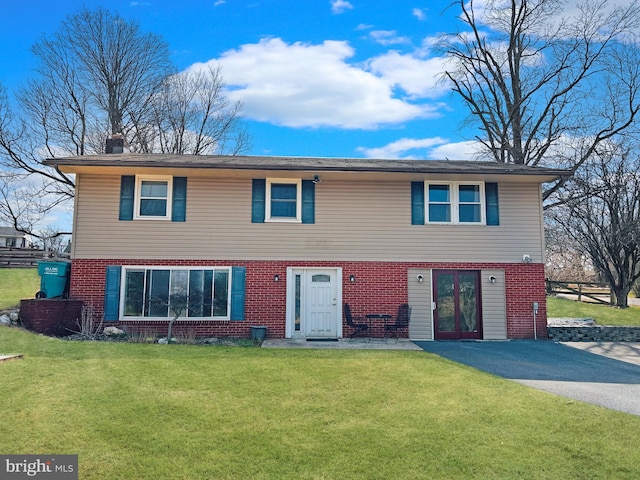 view of front facade featuring brick siding, a chimney, aphalt driveway, and a front lawn