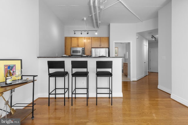 kitchen featuring a breakfast bar area, dark countertops, refrigerator, light wood-style flooring, and stainless steel microwave