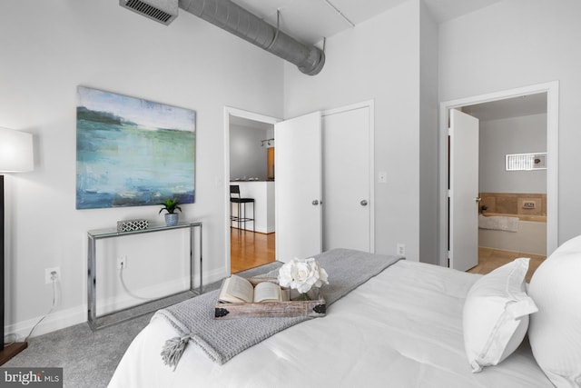 bedroom featuring visible vents, ensuite bath, baseboards, and a towering ceiling