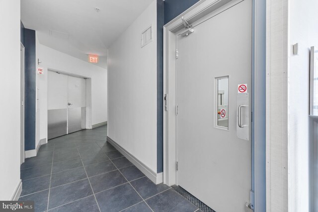 hallway with visible vents, baseboards, and dark tile patterned flooring