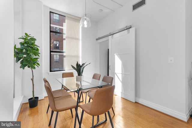 dining space with a barn door, light wood-style flooring, baseboards, and visible vents