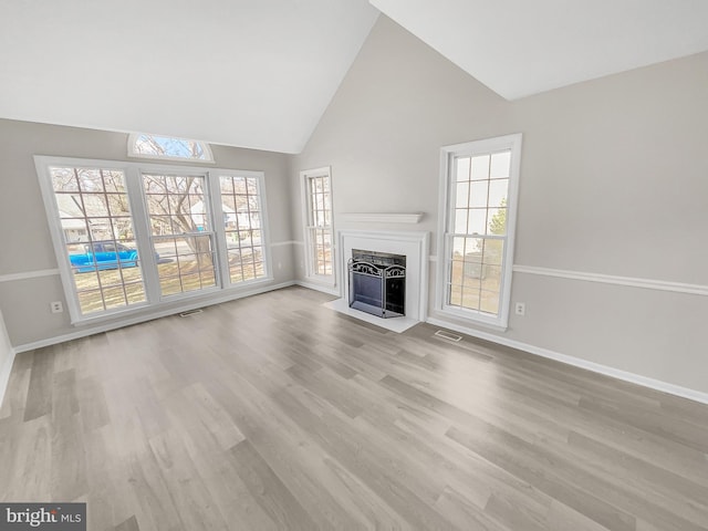 unfurnished living room featuring plenty of natural light, wood finished floors, visible vents, and a fireplace with flush hearth