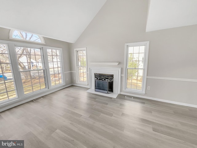 unfurnished living room featuring visible vents, a fireplace with flush hearth, high vaulted ceiling, wood finished floors, and baseboards