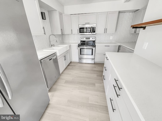 kitchen with a sink, stainless steel appliances, light wood-style flooring, and decorative backsplash