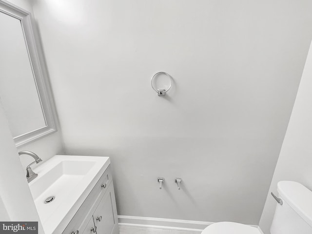 half bath with baseboards, toilet, and vanity