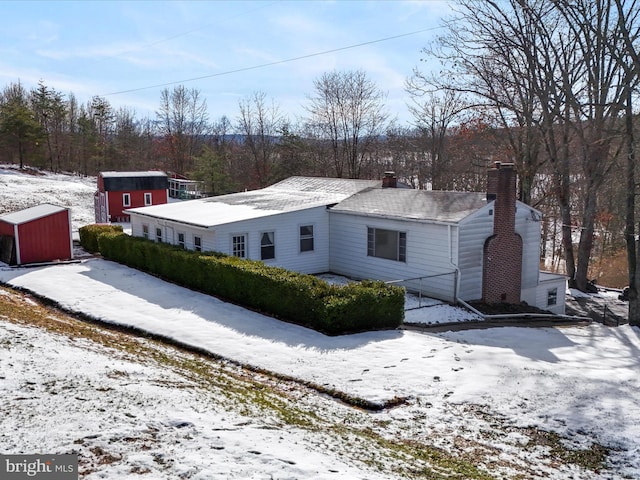 snow covered property with a storage unit, a chimney, and an outdoor structure