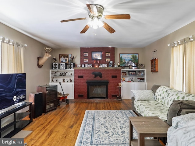 living area with a fireplace, ceiling fan, and wood finished floors