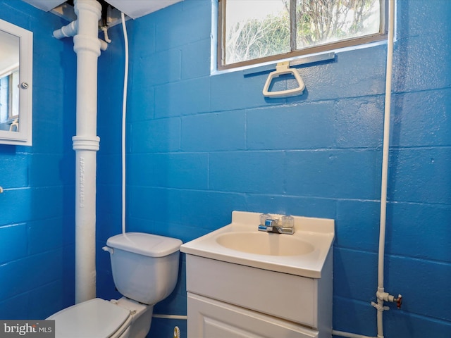 bathroom featuring concrete block wall, toilet, and vanity