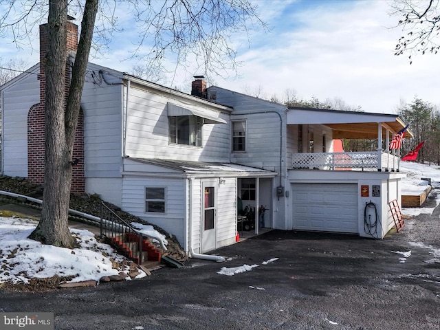 back of house featuring aphalt driveway, a chimney, and a garage