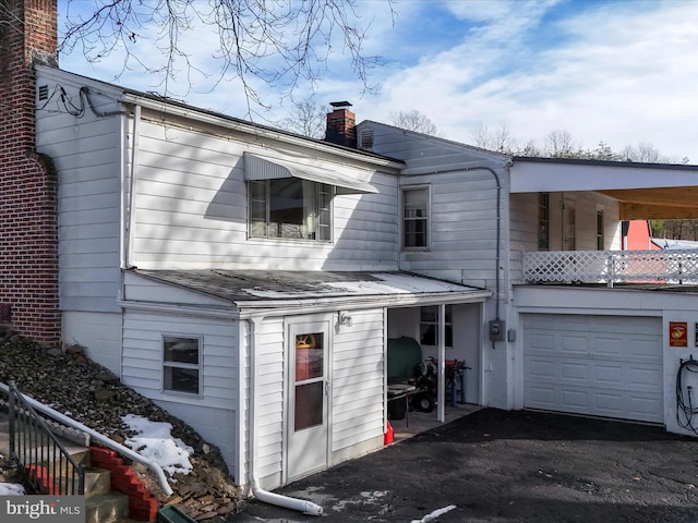 back of house with a garage, a chimney, and a shingled roof