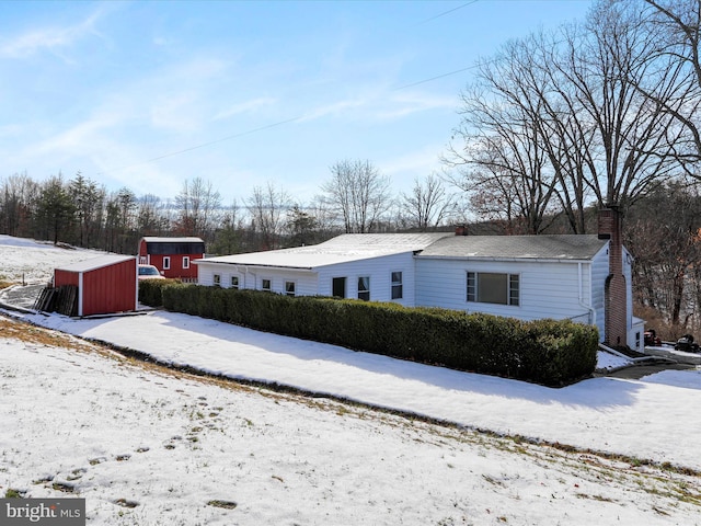 snow covered property with a chimney, a storage shed, and an outdoor structure