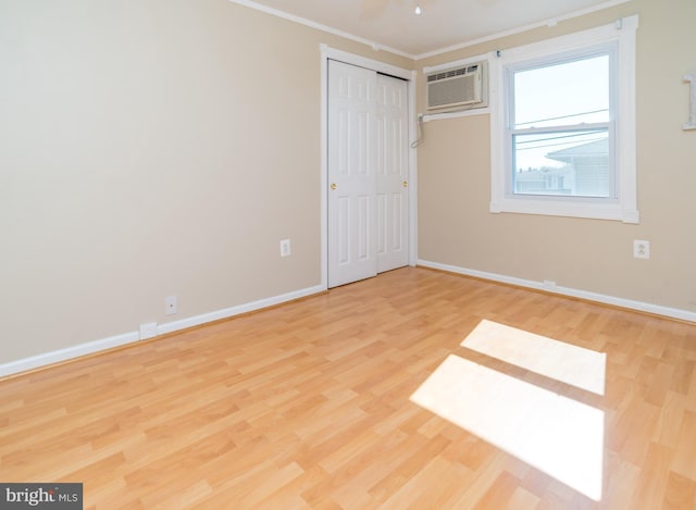 unfurnished bedroom with a wall unit AC, a ceiling fan, baseboards, light wood-style floors, and crown molding