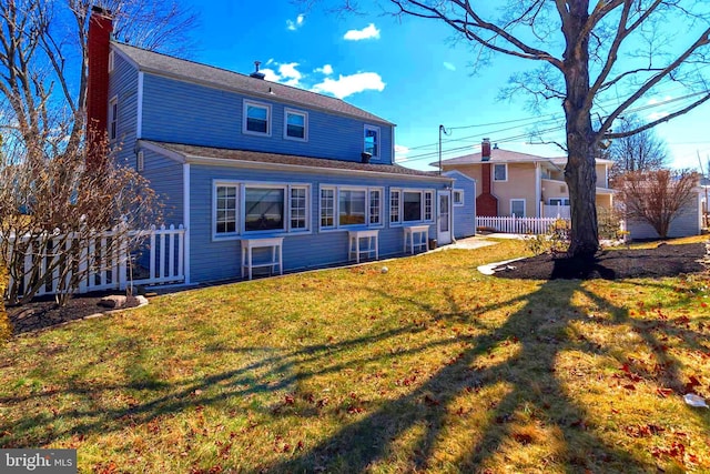 rear view of property with a yard, a chimney, and fence