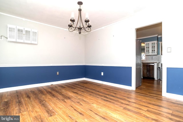 unfurnished room featuring ornamental molding, wood finished floors, baseboards, and a chandelier