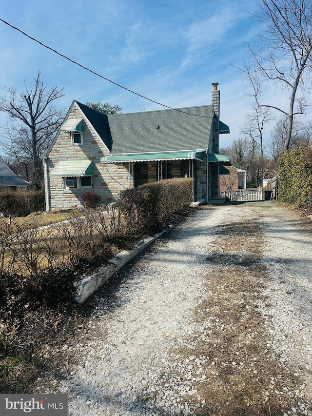 view of side of property with gravel driveway, stone siding, and a chimney