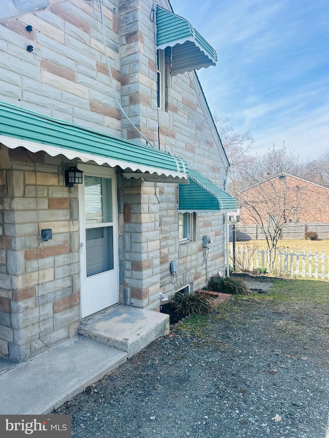 property entrance featuring fence and stone siding