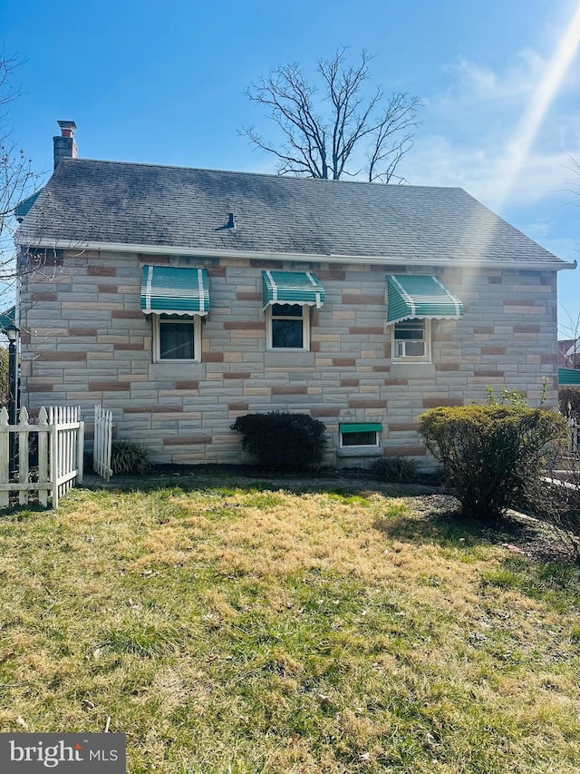 back of property with stone siding, a lawn, a chimney, and fence