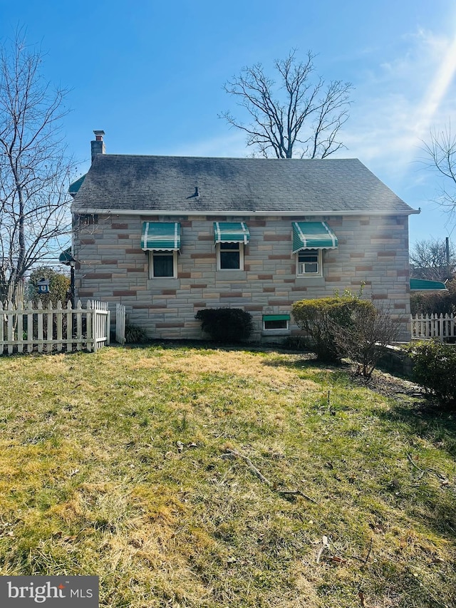 rear view of house with a yard, stone siding, a chimney, and fence