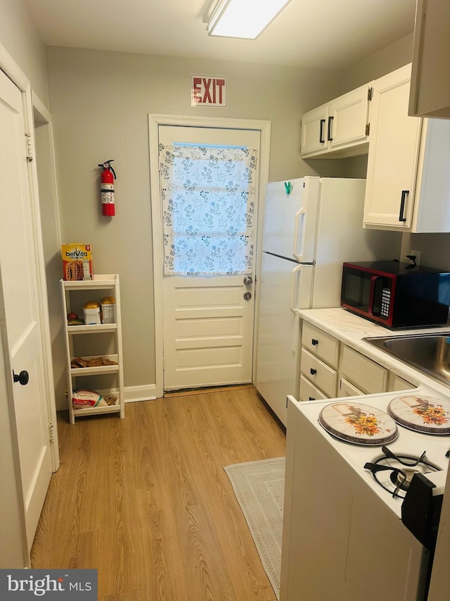 kitchen with light wood finished floors, black microwave, light countertops, white cabinets, and white electric range