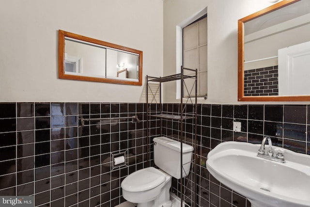 half bathroom featuring a wainscoted wall, toilet, tile walls, and a sink