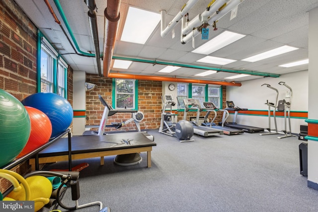 gym with a drop ceiling and brick wall