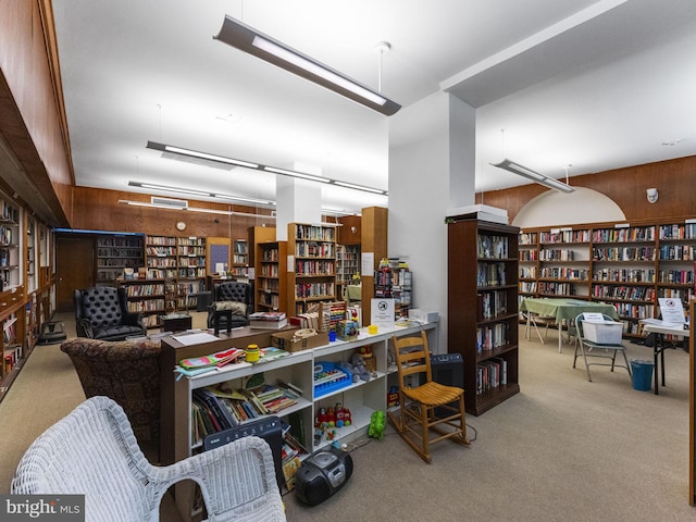 misc room with wooden walls, carpet flooring, and wall of books