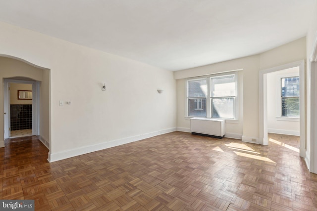 spare room with arched walkways, radiator, and baseboards