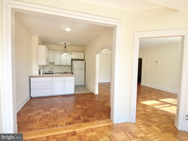 kitchen featuring baseboards, light countertops, a peninsula, freestanding refrigerator, and white cabinetry