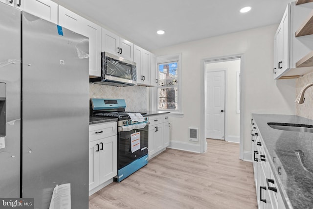 kitchen with visible vents, a sink, open shelves, stainless steel appliances, and dark stone counters