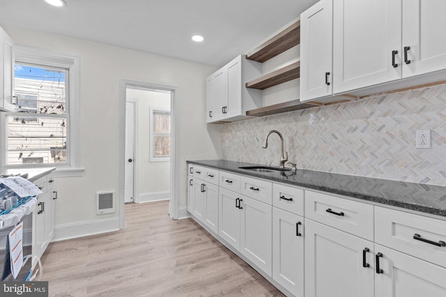 kitchen featuring a sink, open shelves, dark stone countertops, white cabinetry, and light wood finished floors