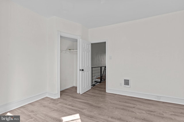 unfurnished bedroom featuring wood finished floors, visible vents, a closet, and baseboards