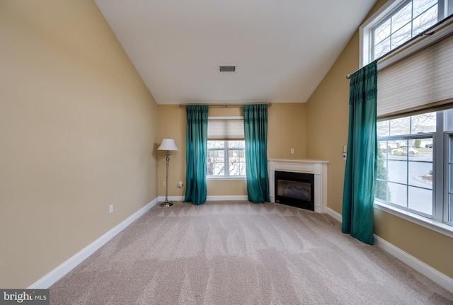 unfurnished living room featuring a glass covered fireplace, lofted ceiling, carpet, and visible vents