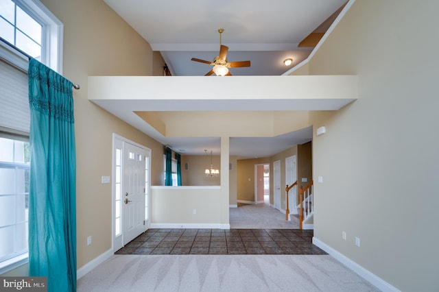 carpeted foyer featuring stairs, ceiling fan with notable chandelier, baseboards, and a towering ceiling