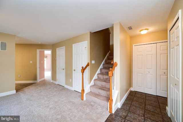 entryway with visible vents, dark carpet, stairs, and baseboards