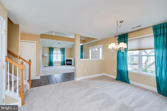 unfurnished room with visible vents, carpet floors, a fireplace, a chandelier, and stairs