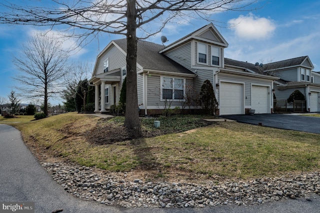 traditional-style home featuring aphalt driveway, an attached garage, a front lawn, and a shingled roof