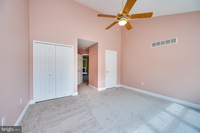 unfurnished bedroom featuring visible vents, baseboards, carpet floors, a towering ceiling, and a closet