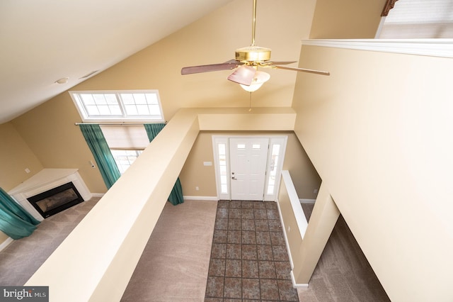 carpeted foyer entrance with a glass covered fireplace, high vaulted ceiling, baseboards, and a ceiling fan