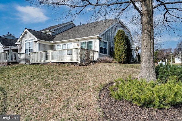 exterior space with a deck, a front yard, and a shingled roof