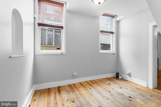 empty room featuring baseboards, arched walkways, and hardwood / wood-style floors