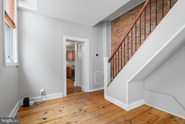 interior space featuring visible vents, hardwood / wood-style floors, brick wall, baseboards, and stairs