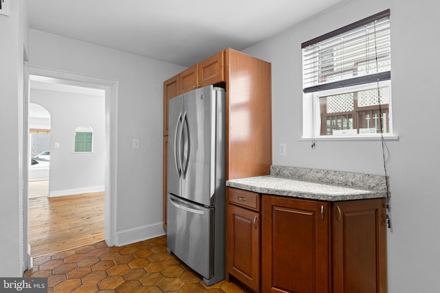 kitchen with a wealth of natural light, brown cabinets, arched walkways, and freestanding refrigerator