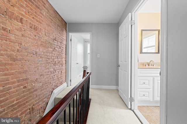 corridor featuring an upstairs landing, light colored carpet, brick wall, and a sink