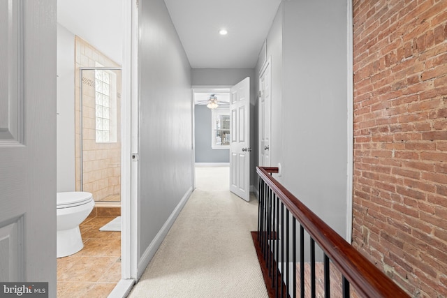 hall featuring an upstairs landing, tile patterned floors, brick wall, and baseboards