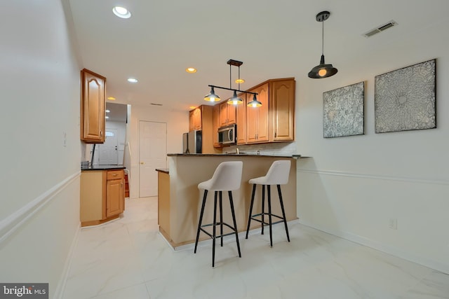 kitchen featuring visible vents, stainless steel microwave, dark countertops, a peninsula, and a breakfast bar area