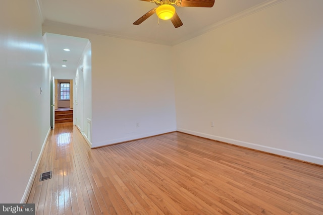 empty room featuring crown molding, light wood-style flooring, baseboards, and visible vents